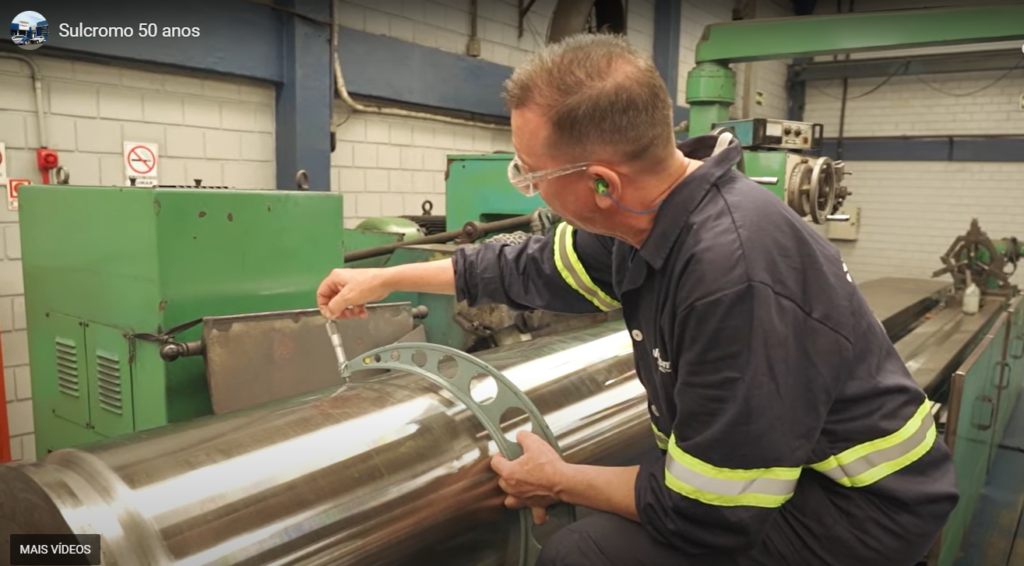 Trabalhador operando uma retífica industrial cilíndrica, realizando o processo de acabamento preciso em uma peça metálica, garantindo a qualidade e precisão exigidas na indústria.